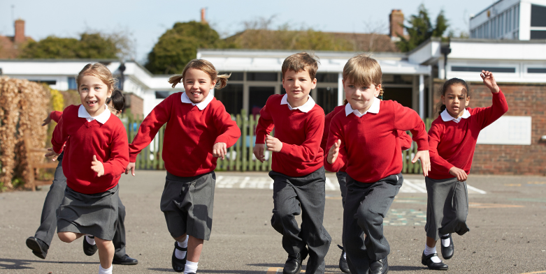 An image of school children in uniform, wearing red jumpers and running across the playground towards the camera