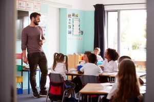 Male teacher, teaching a class room of young children, in a primary school setting.